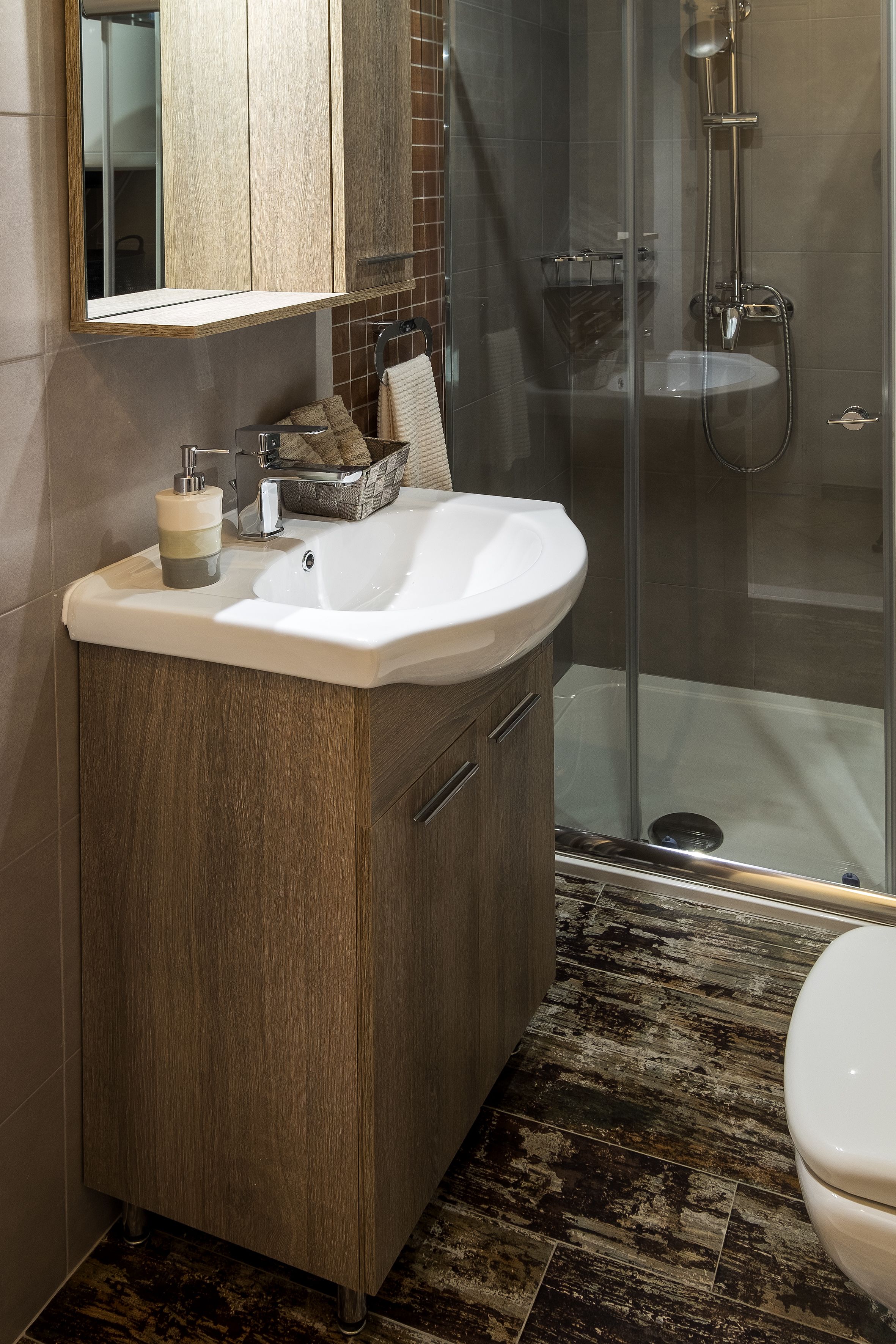 A modern bathroom with a wooden vanity, a glass shower enclosure, and a marble-tiled floor.