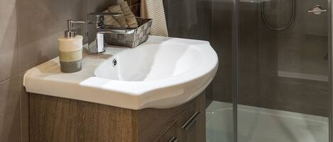 A modern bathroom with a wooden vanity, a glass shower enclosure, and a marble-tiled floor.