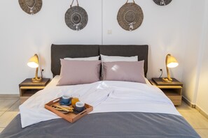 A neatly made bed with a tray of breakfast items, two bedside lamps, and decorative wall art. - Paros Nereids Villas (Paros)
