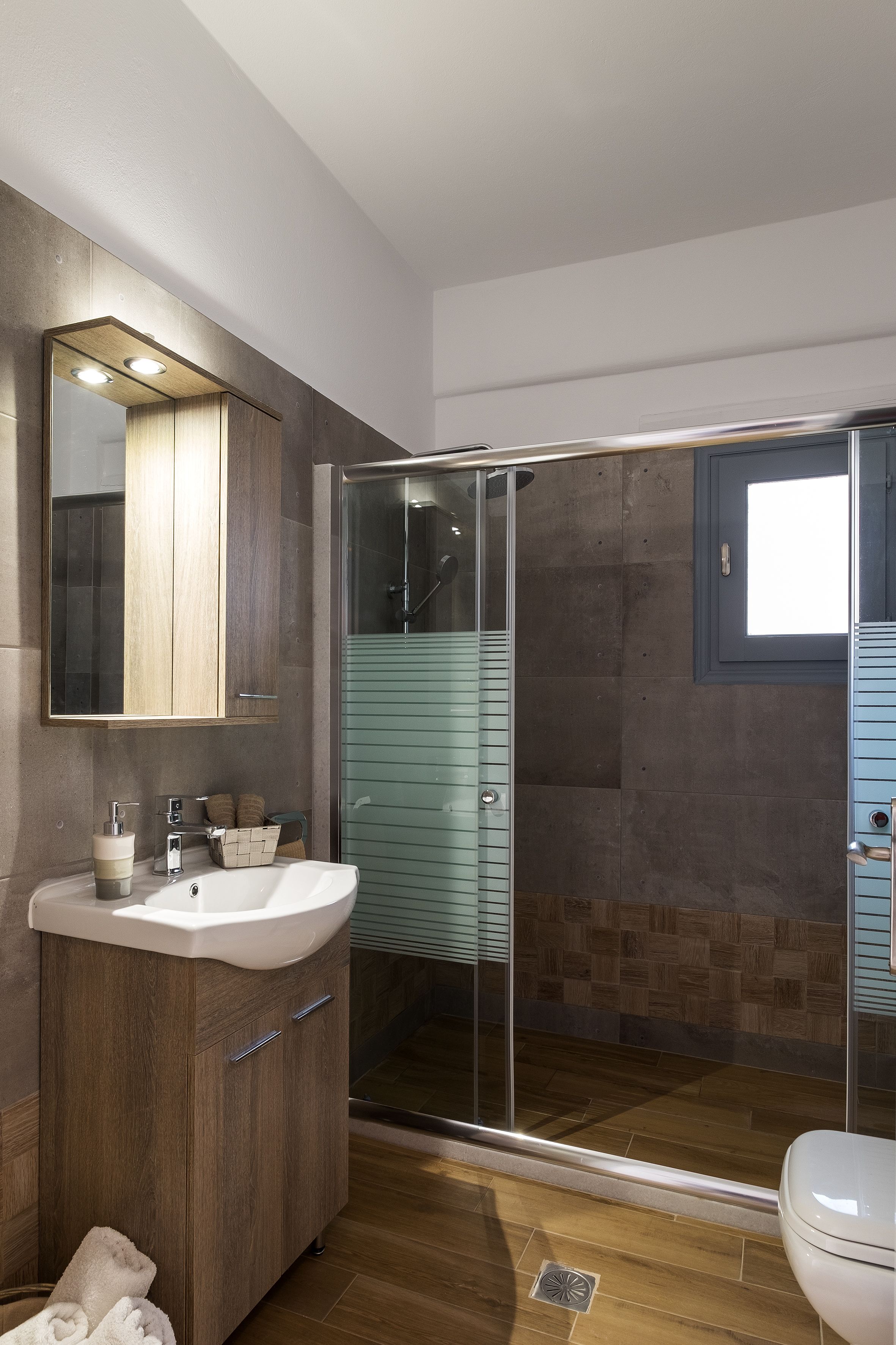 A modern bathroom with a wooden vanity, a glass shower enclosure, and a white toilet.