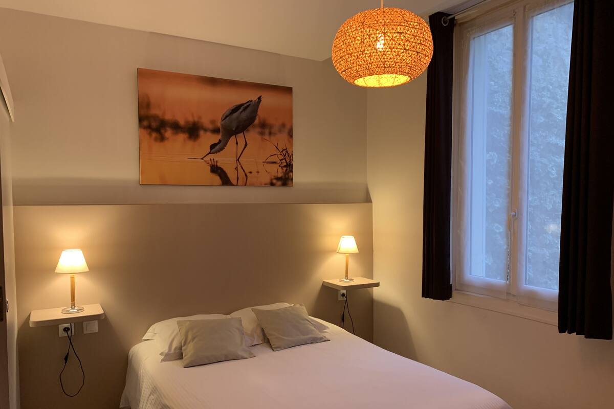 Un dormitorio con cama, dos lámparas de noche, un cuadro en la pared y una ventana con cortinas.