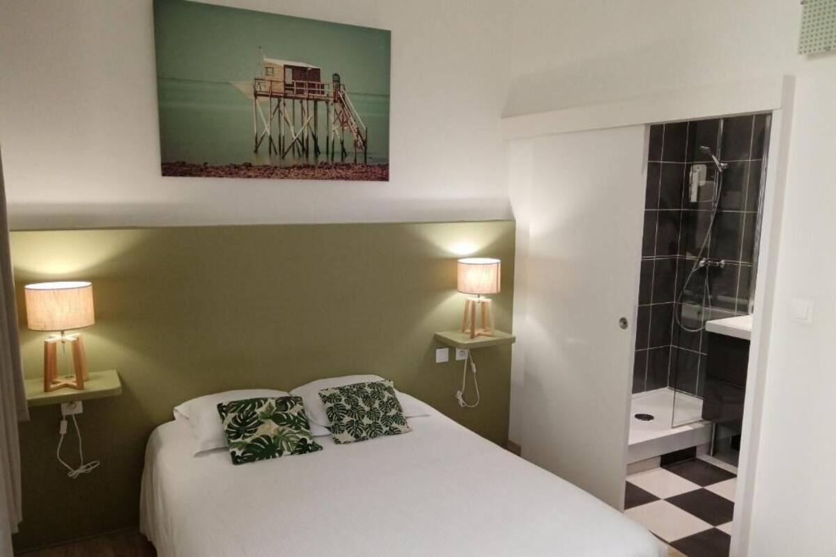Habitación de hotel con una cama, dos lámparas de noche, un cuadro de un muelle y una zona de ducha.