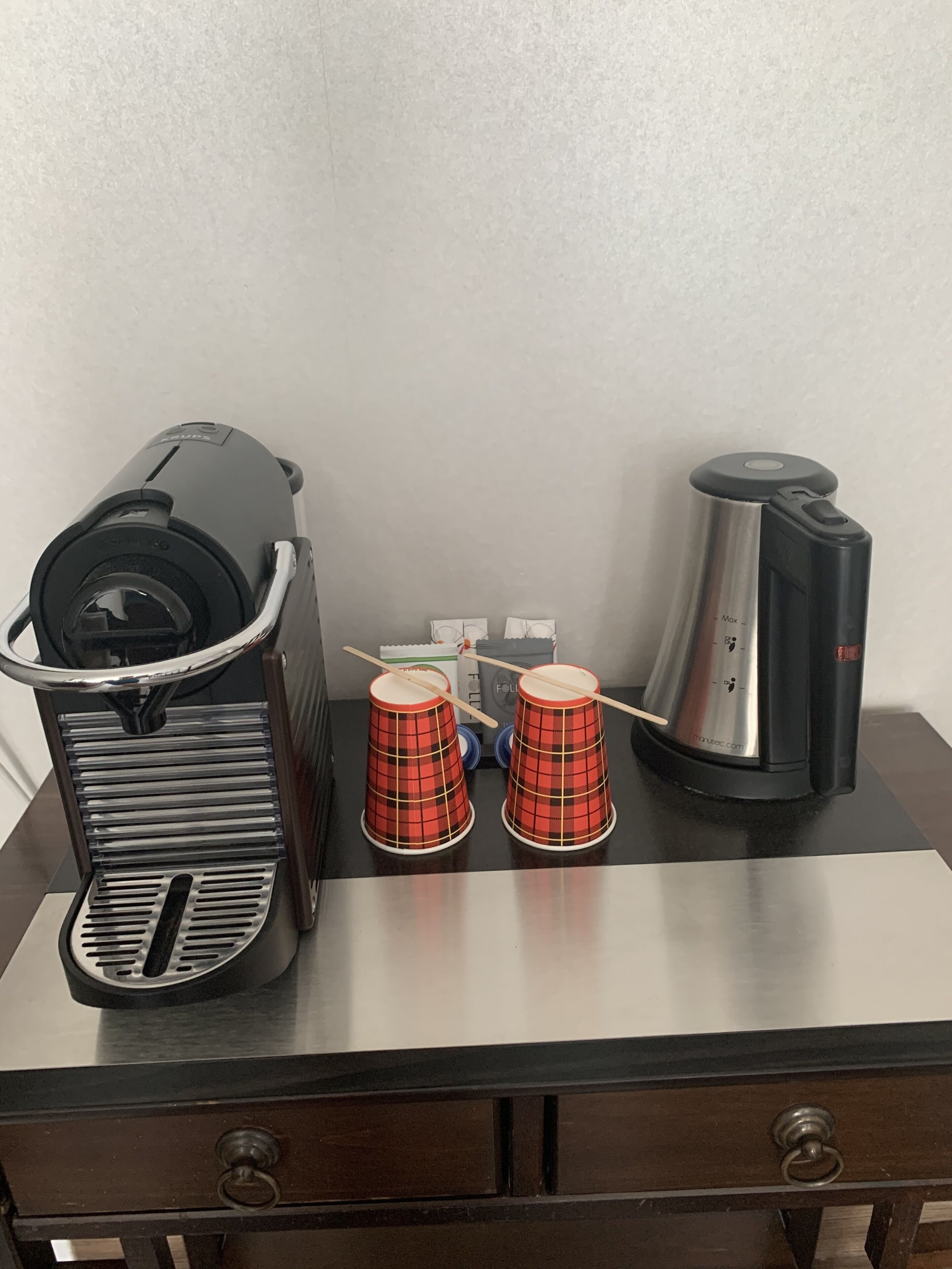 Eine Kaffeemaschine, zwei rot karierte Tassen und eine Kaffeekanne auf einem Tisch.