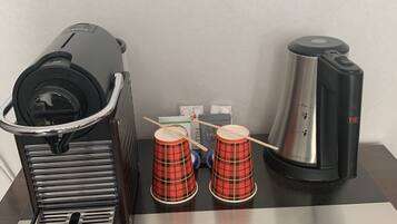 Eine Kaffeemaschine, zwei rot karierte Tassen und eine Kaffeekanne auf einem Tisch.