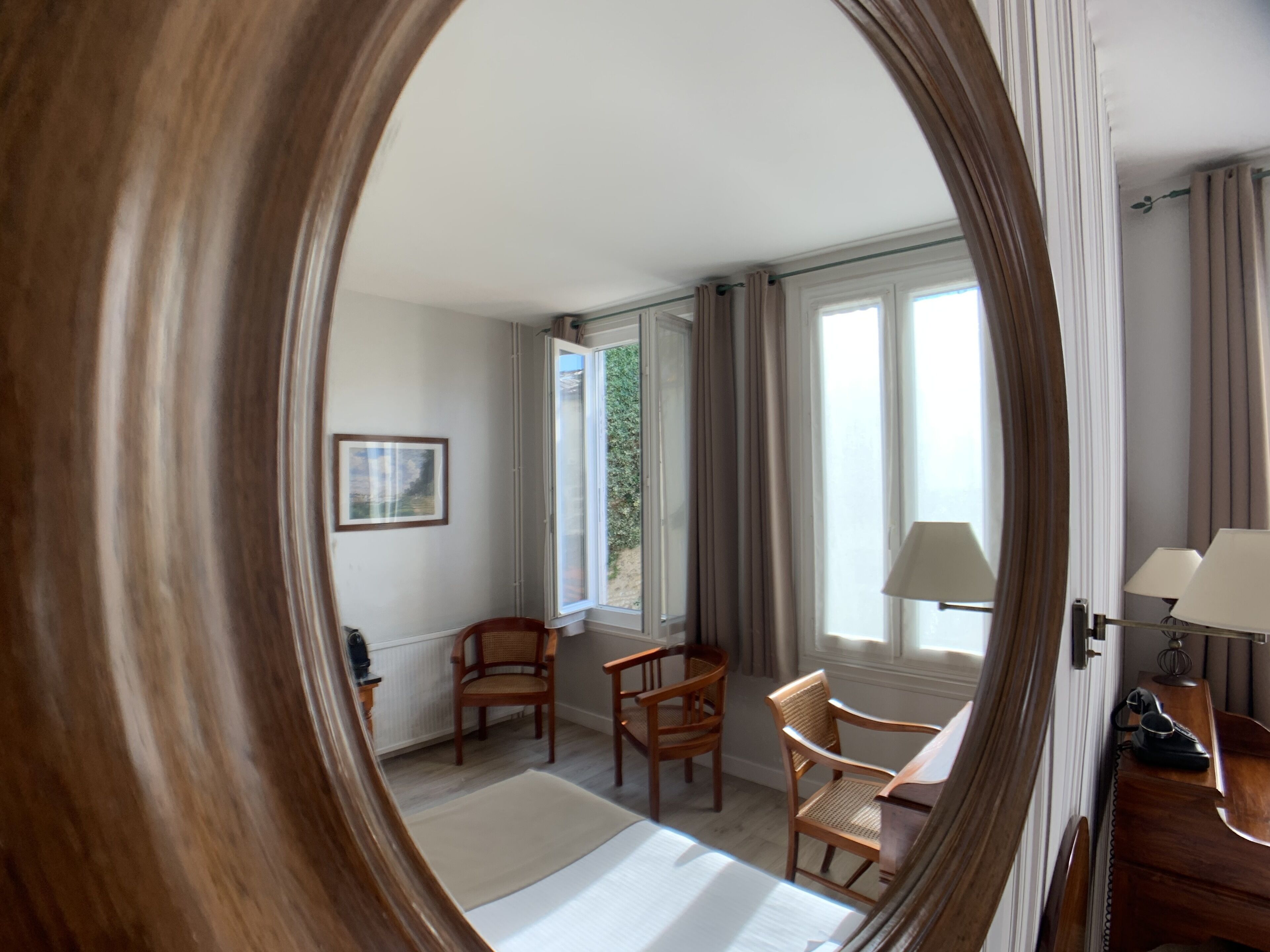 A room with a bed, two chairs, a desk with a lamp, and a window with curtains.