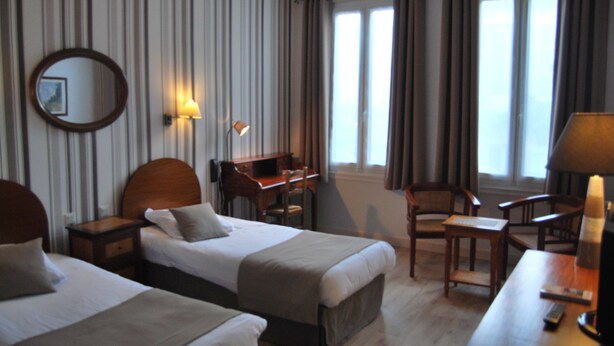 Een hotelkamer met twee bedden, een bureau, een stoel, een lamp en een spiegel.