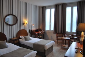 Een hotelkamer met twee bedden, een bureau, een stoel, een lamp en een spiegel.