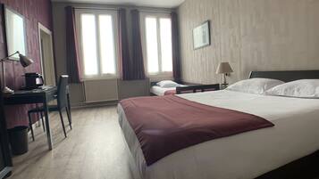 Habitación de hotel con una cama grande, un escritorio con silla, un radiador y dos ventanas con cortinas.