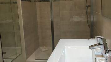 A modern bathroom with a glass-enclosed shower, a white sink, and a towel on the counter.