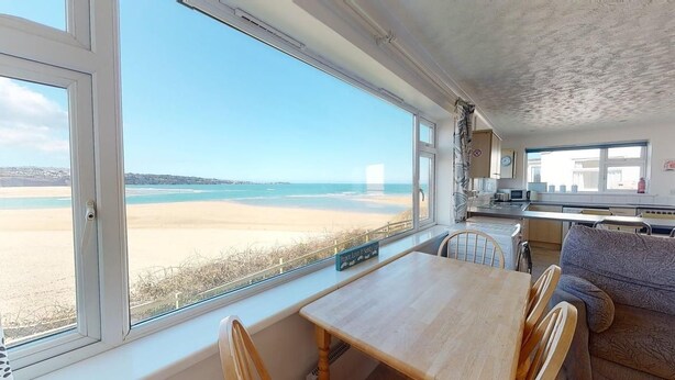 Quarto com uma janela grande com vista para a praia, uma mesa de jantar com cadeiras, um sofá e uma área de cozinha.