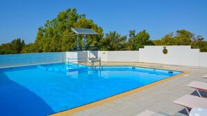 Una piscina con piattaforma tuffatori e area coperta, circondata da un muro bianco e alberi.