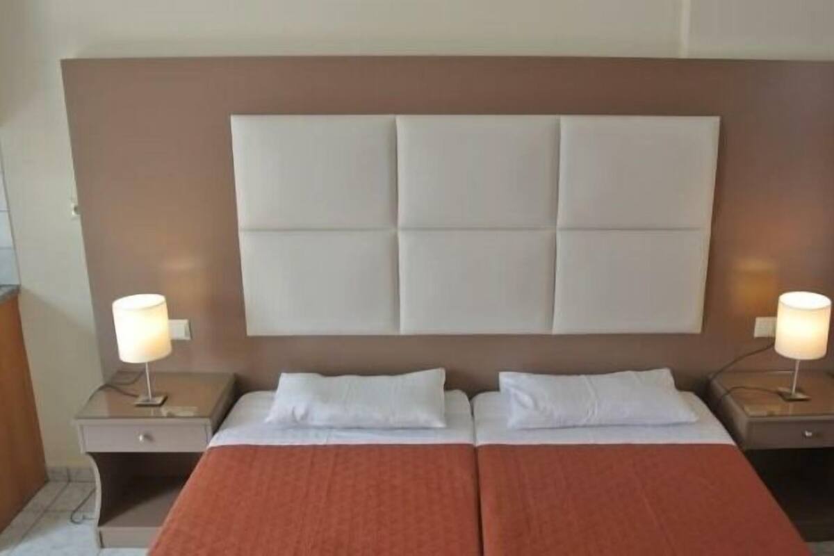 A double bed with a padded headboard, two bedside tables with lamps, and a red blanket.