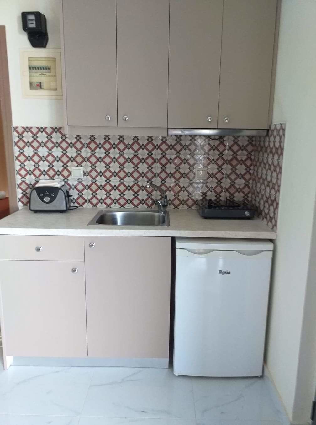 A compact kitchen with a sink, a toaster, a small refrigerator, and patterned backsplash tiles.