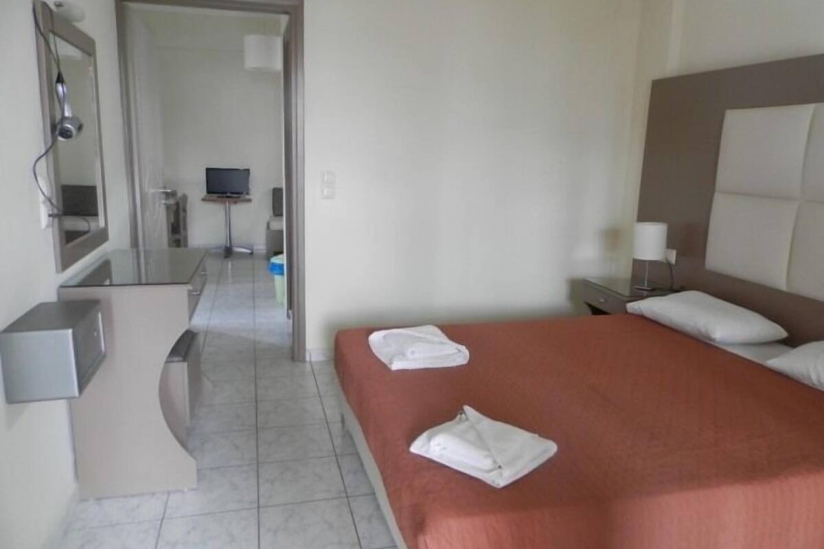 A hotel room with a bed, a desk, a mirror, a TV, and a bathroom visible through an open door.