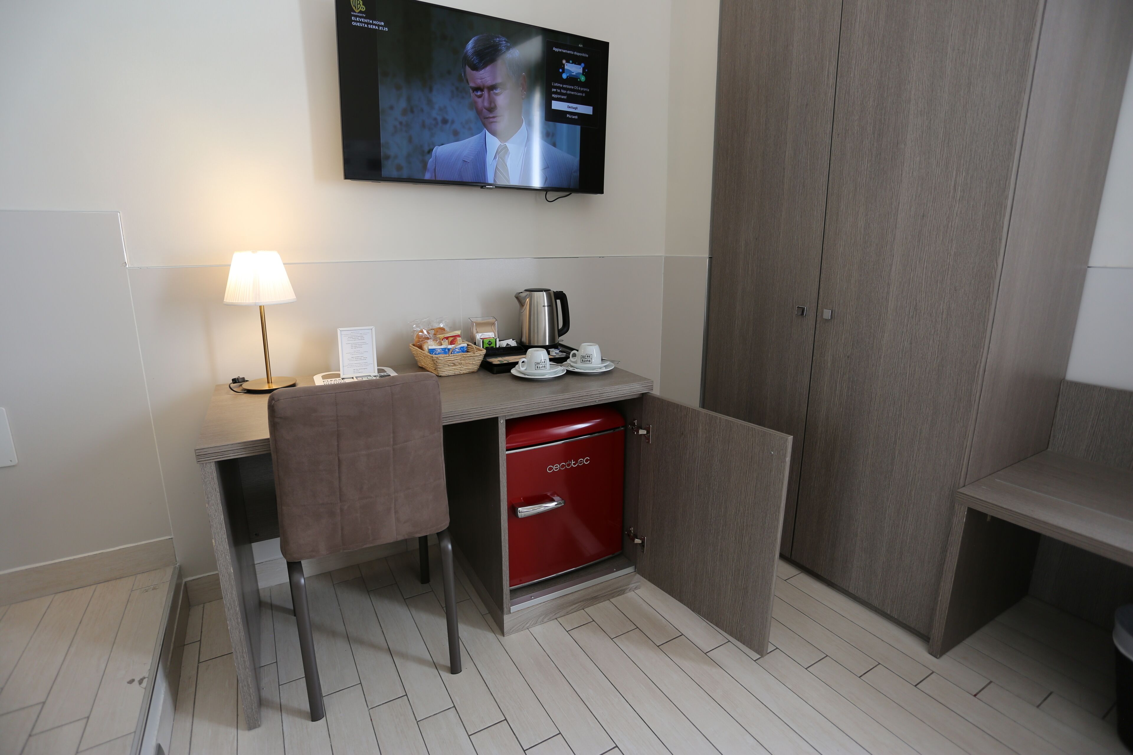 Une chambre d’hôtel équipée d’un bureau, d’une télévision, d’un mini-bar rouge, d’une lampe et d’un coin salon.
