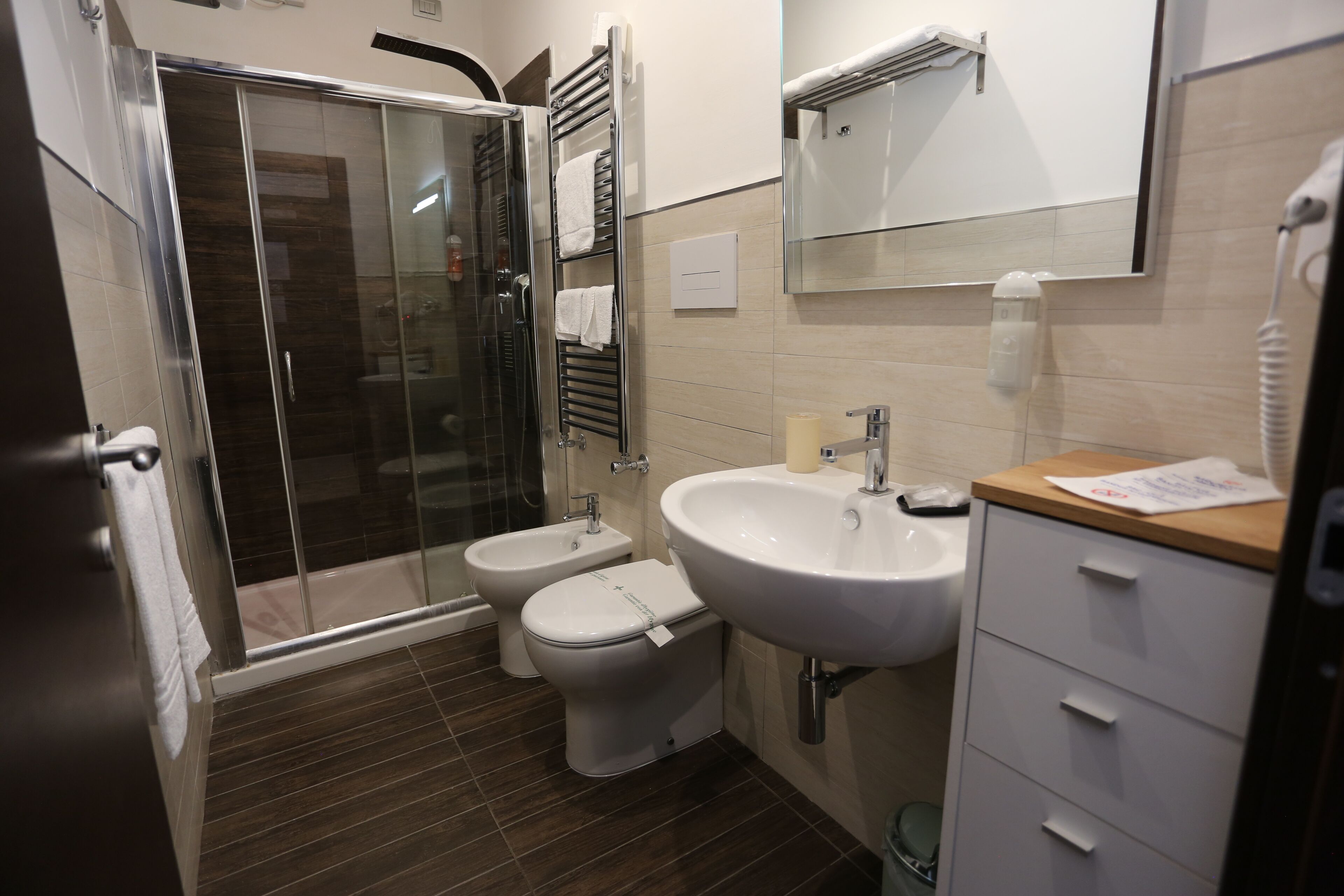 A modern bathroom with a glass-enclosed shower, a bidet, a toilet, a sink, and a mirror.