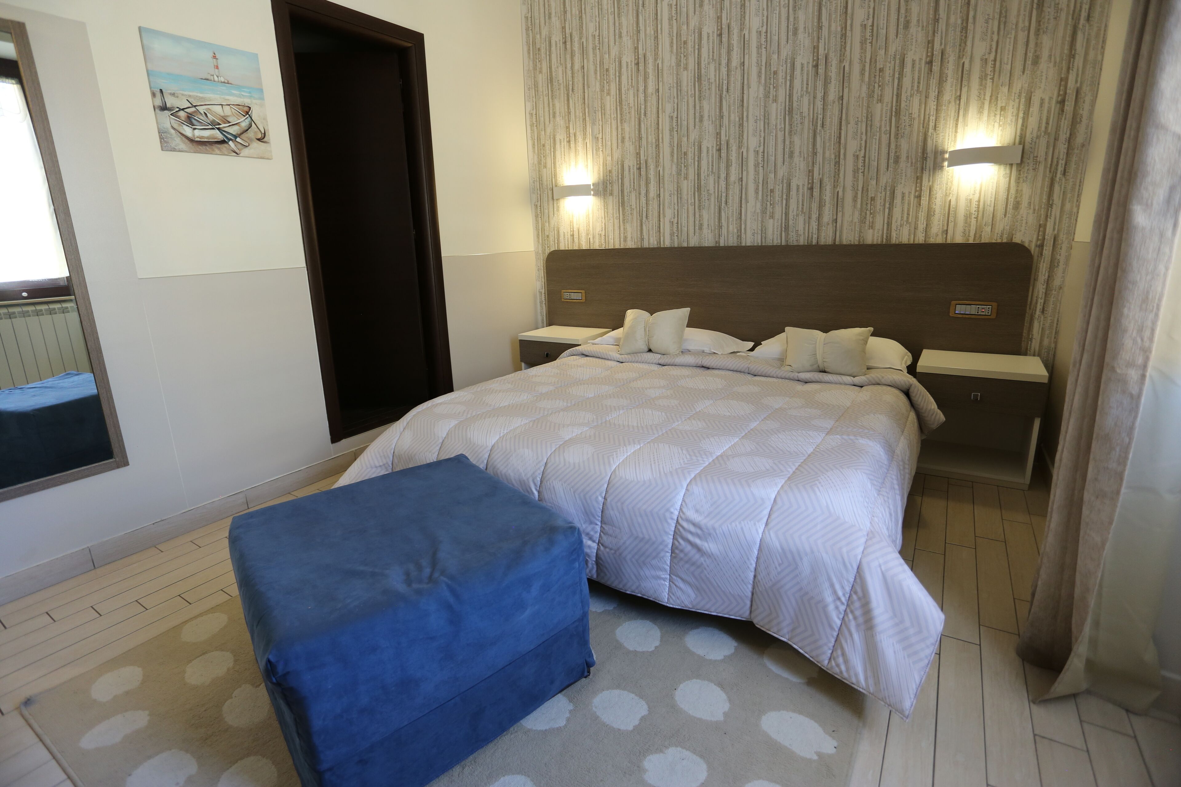 Een slaapkamer met een bed, een nachtkastje, een bankje, een schilderij en een wandlamp.