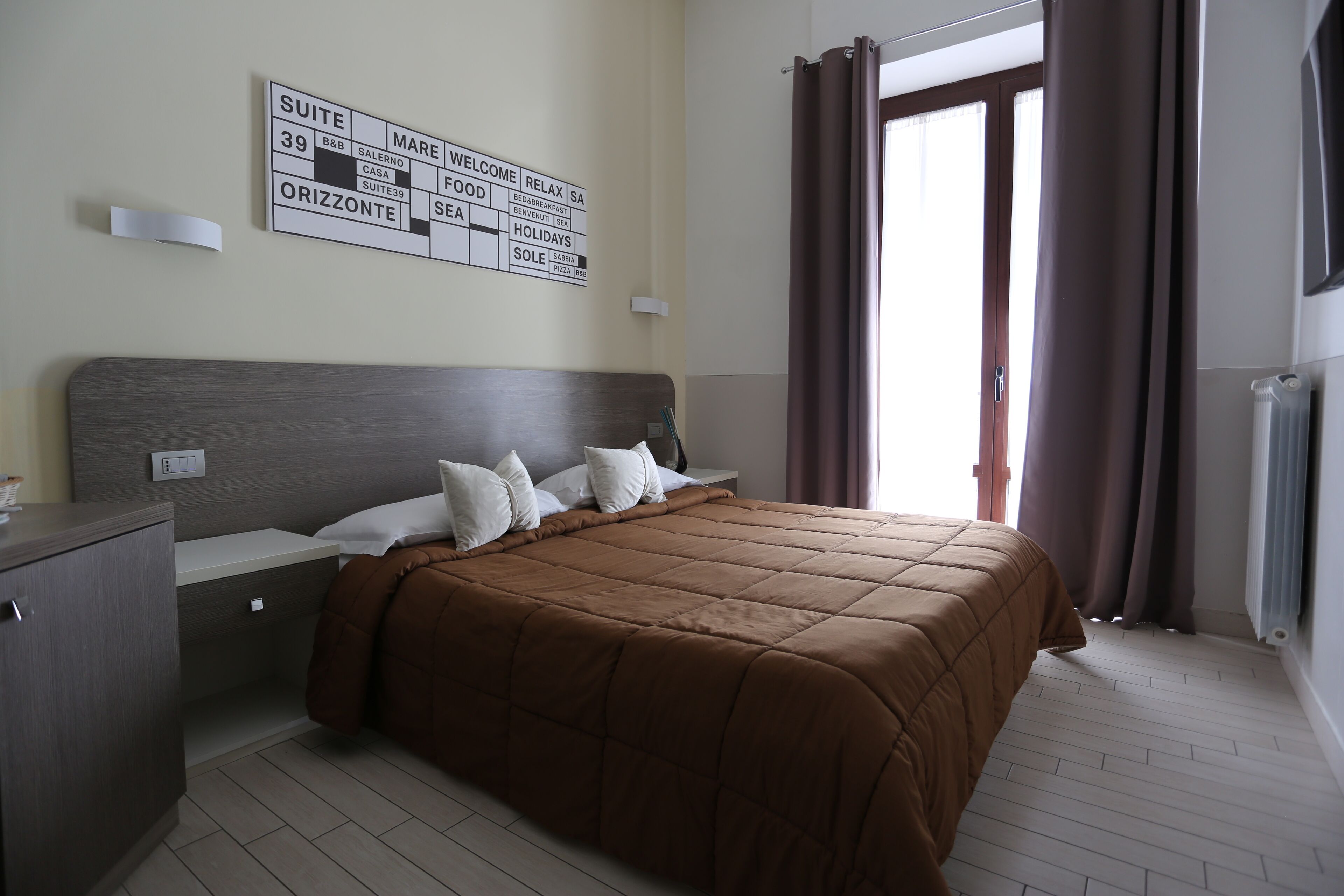 A bedroom with a large bed, a nightstand, a dresser, and a wall sign with room names and amenities.