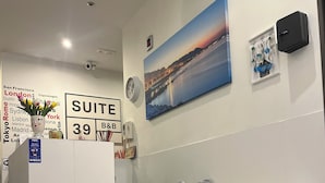 A reception area with a white desk, a sofa with a pillow, a painting of a sunset, and a sign indicating the suite number 39. - Suite 39 Guest House (Salerno)