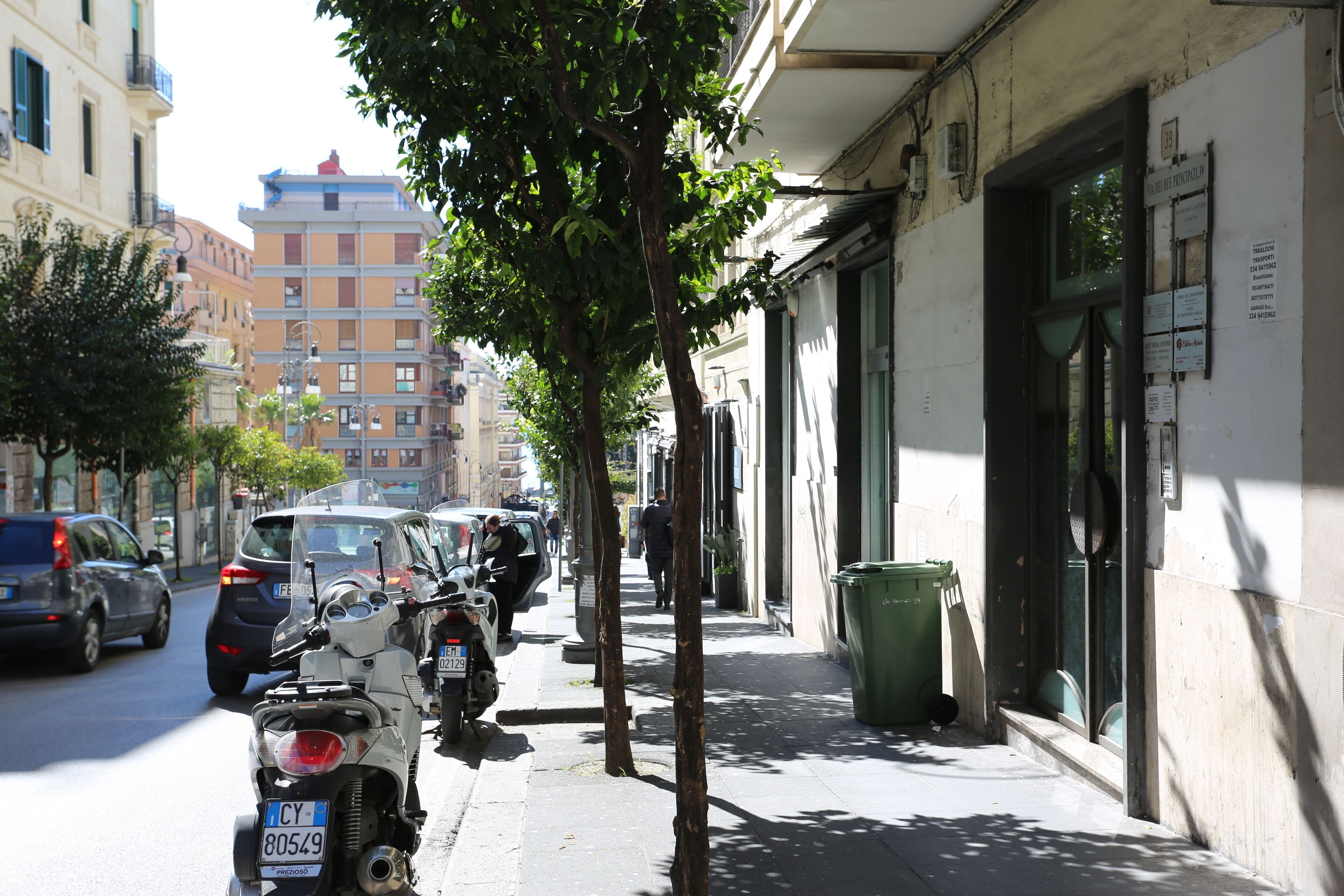 A street with parked motorcycles and cars, a sidewalk, and buildings with signage.