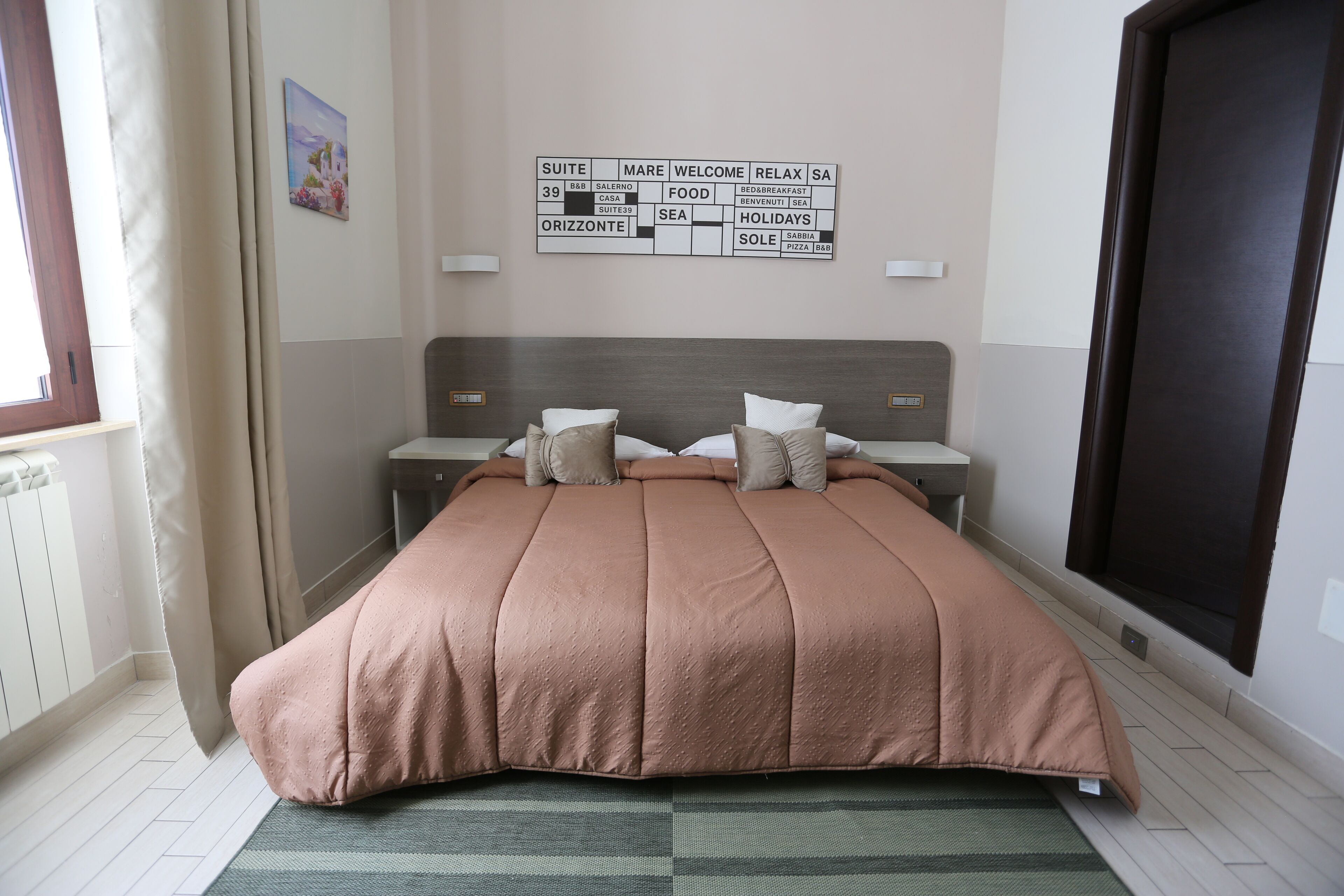 A bedroom with a large bed, a headboard, a bedside table, and a wall-mounted sign with various words.