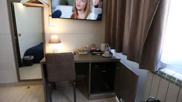 Habitación de hotel con escritorio, silla, televisor, lámpara y una pequeña zona de kitchenette.