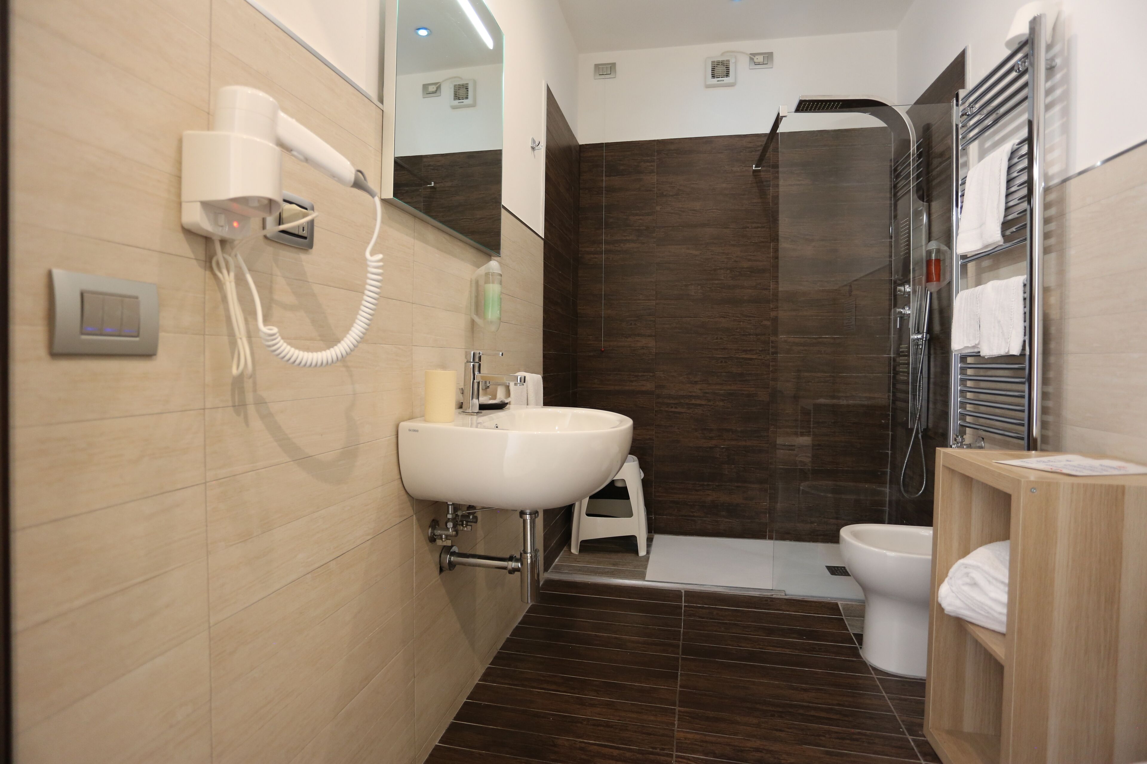 Un baño moderno con lavamanos, espejo, secador de pelo, ducha e inodoro.