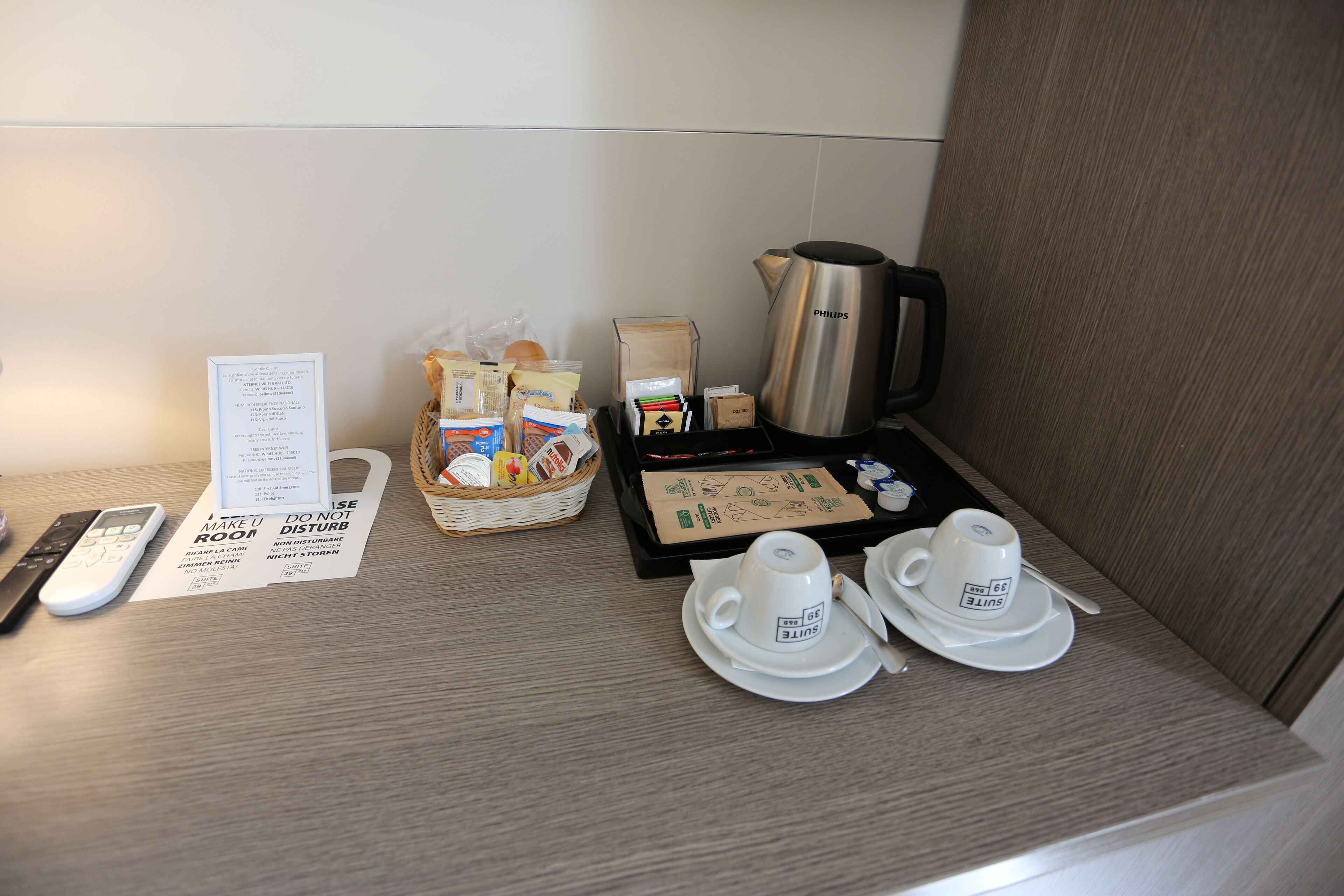 Angolo colazione in una camera d'albergo, con macchina del caffè, set da tè e vari prodotti per la colazione sul mobile.