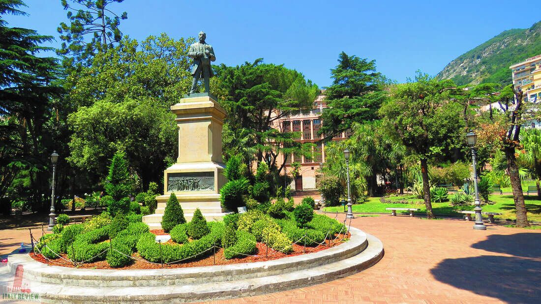 Una estatua en un área ajardinada con bancos y árboles.