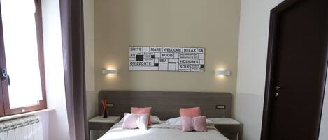 Ein Hotelzimmer mit Bett, zwei Nachttischen, einem an der Wand befestigten Schild mit Informationen zu den Zimmerausstattungen, einem Fenster mit Vorhängen und einer Tür.
