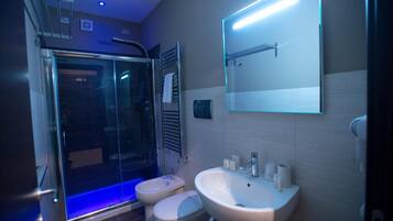Un baño moderno con cabina de ducha de vidrio, inodoro y lavabo con espejo superior.