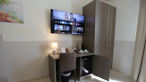 A hotel room with a TV displaying a live stream, a desk with a chair, a lamp, and a small kitchenette area. - Suite 39 Guest House (Salerno)