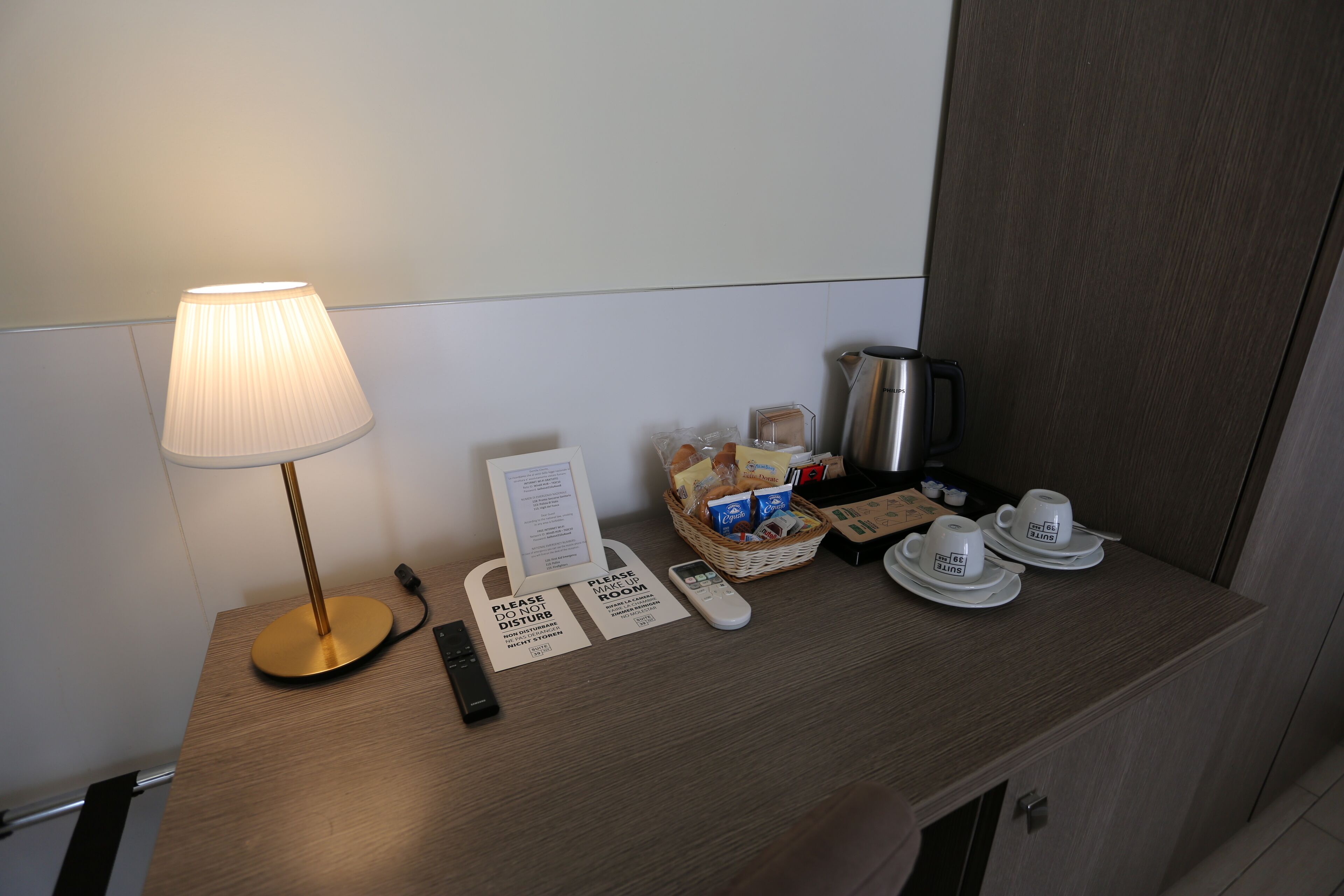 Een bureau in een hotelkamer met een lamp, een mandje met snacks, een koffiezetapparaat en een bordje met de tekst: niet storen.