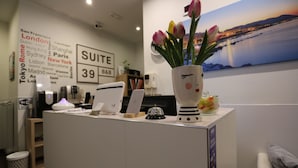 A reception desk with a vase of tulips, a sign with city names, and a painting of a coastal scene. - Suite 39 Guest House (Salerno)