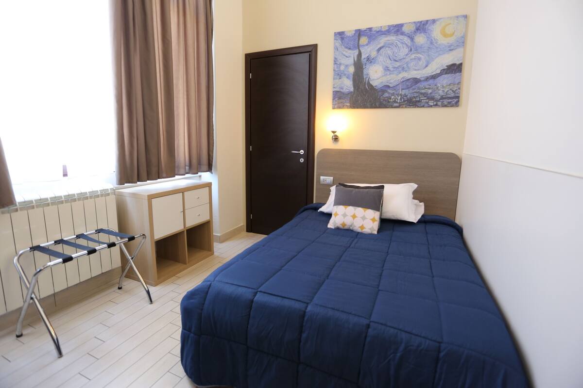 A bedroom with a bed, a desk, and a radiator.
