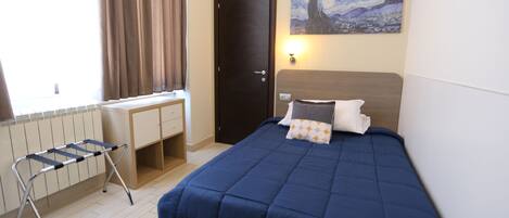 A bedroom with a bed, a desk, and a radiator.