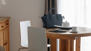 Ein Holztisch mit einem weißen Stuhl, einer schwarzen Handtasche, einem weißen Apfel und einer weißen Tasse.