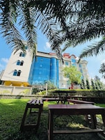 Um edifício com fachada de vidro moderna, seção arquitetônica tradicional e área verde circundante com bancos.