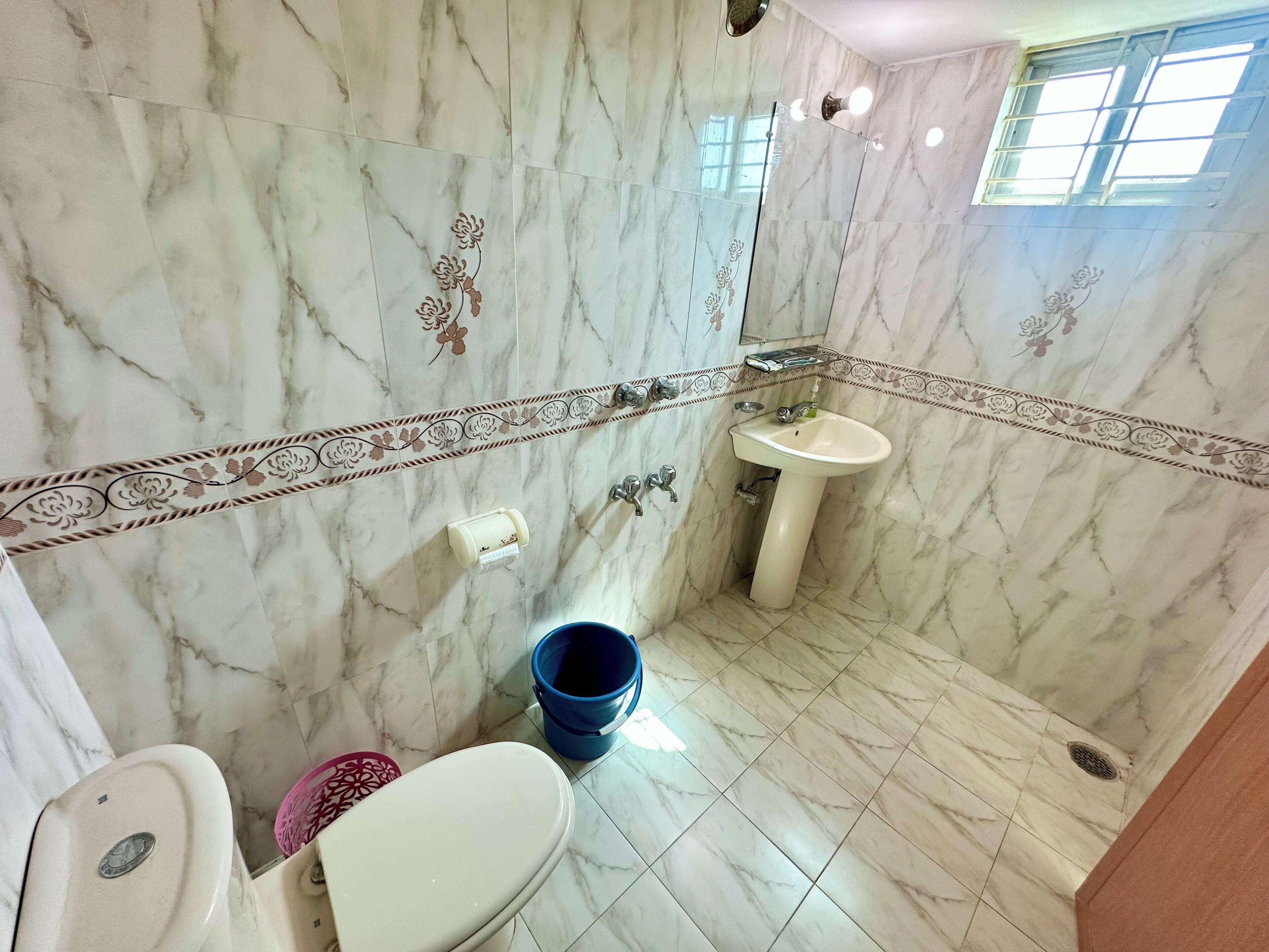 A bathroom with marble walls, a toilet, a sink, and a shower area.