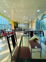 Um espaço amplo e interno com várias mesas e cadeiras, janelas grandes e um teto com padrão único.
