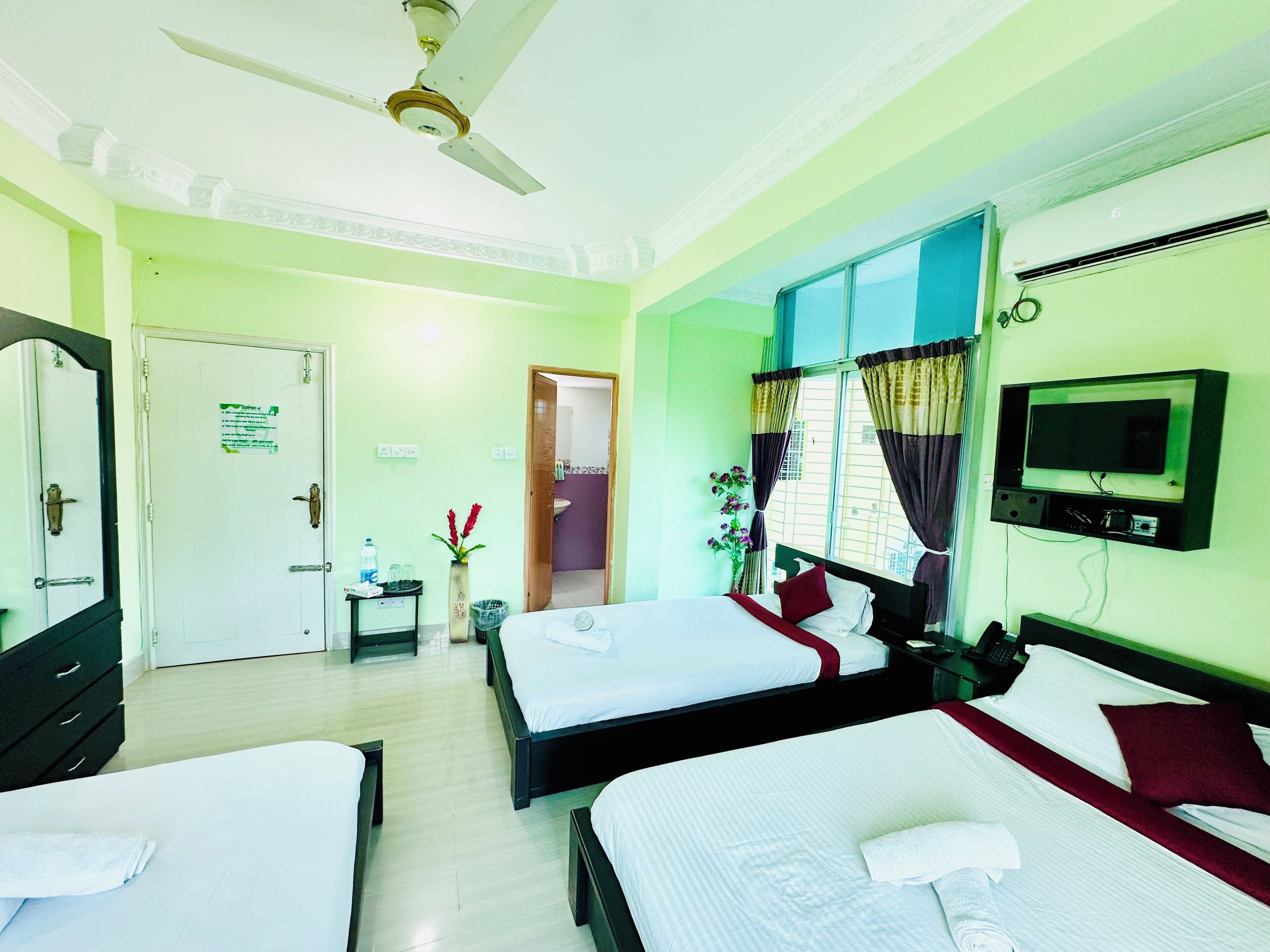 A hotel room with two beds, a ceiling fan, a TV, and a bathroom visible through an open door.