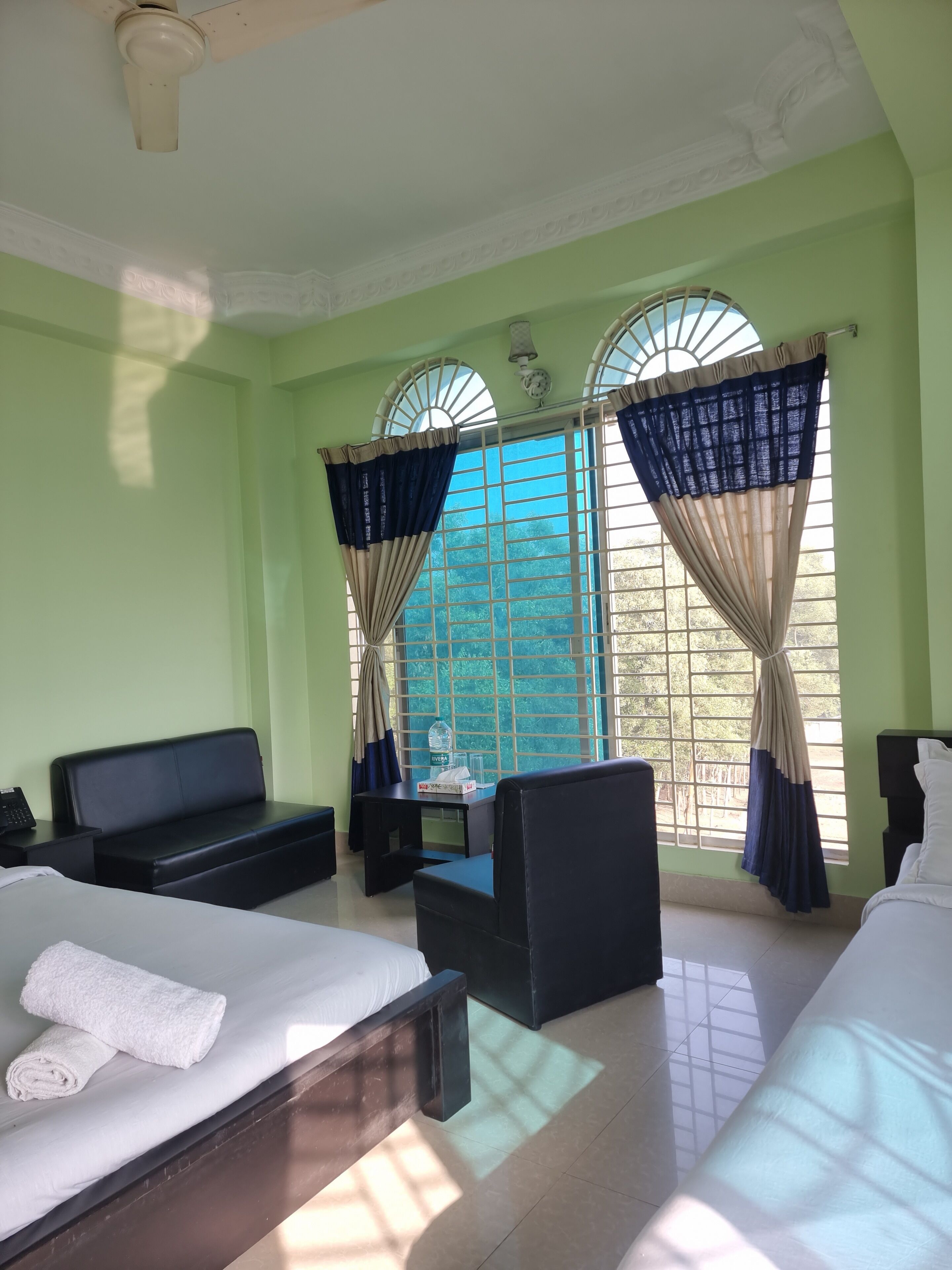 Quarto de hotel com cama, sofá, escrivaninha e duas janelas com cortinas.