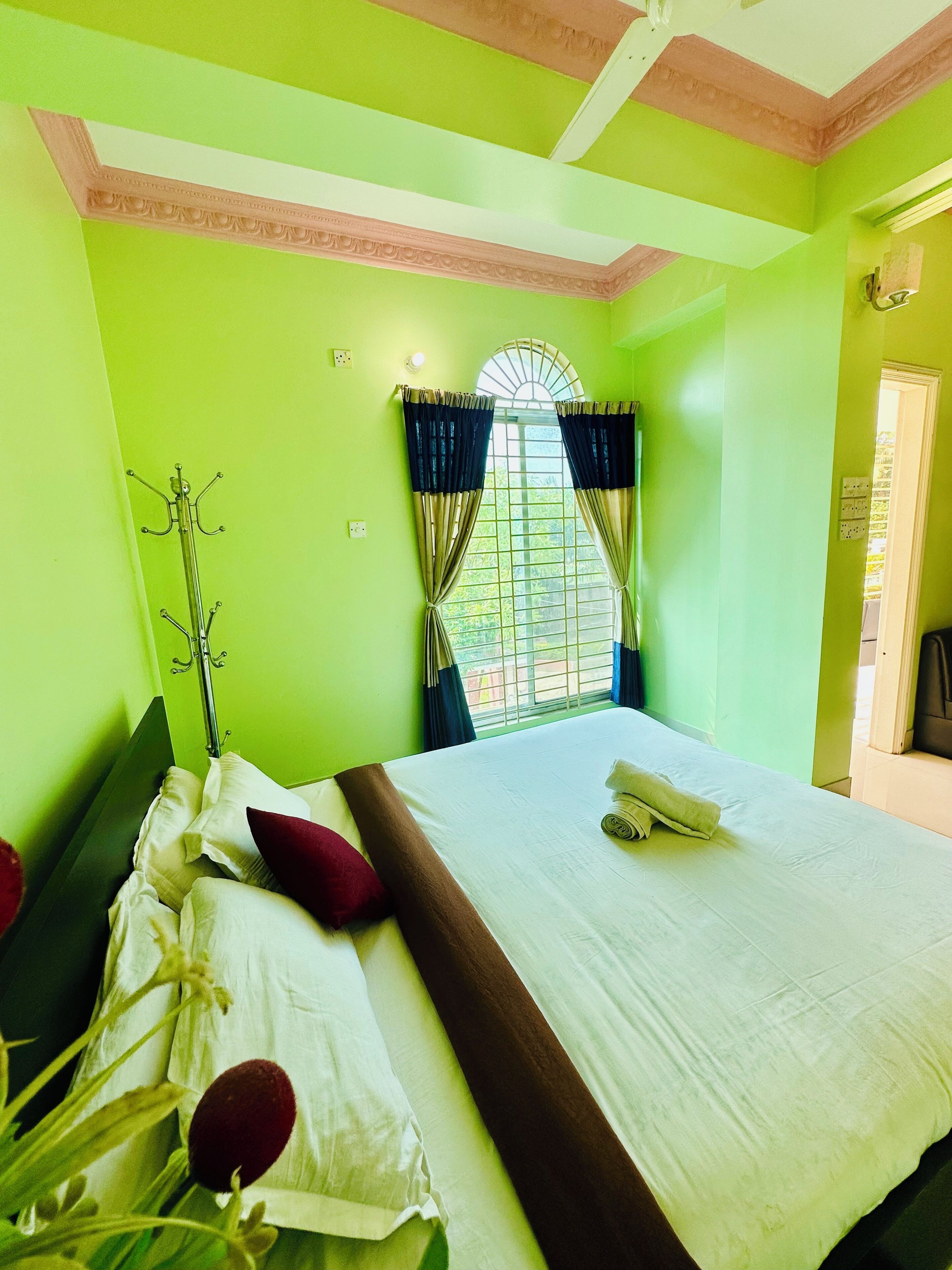 A room with a bed, a window with curtains, a coat rack, and a door.