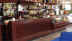 A bar with a counter, shelves of liquor bottles, and a coffee machine. - Grandinetti Hotel (Parenti)