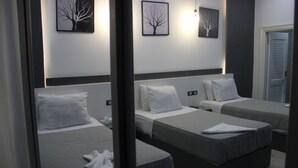 Habitación de hotel con tres camas individuales, cada una con almohada blanca y ropa de cama gris. En la pared, encima de las camas, hay cuadros con imágenes de árboles.