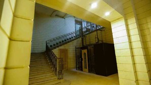 Una escalera que sube a un piso superior con baranda de metal, una puerta al final inferior y un objeto oscuro a la derecha.