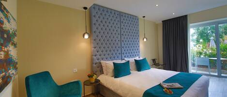 Een slaapkamer met een groot bed, een blauwe stoel, een tafeltje met een vaas, en uitzicht op de omgeving.