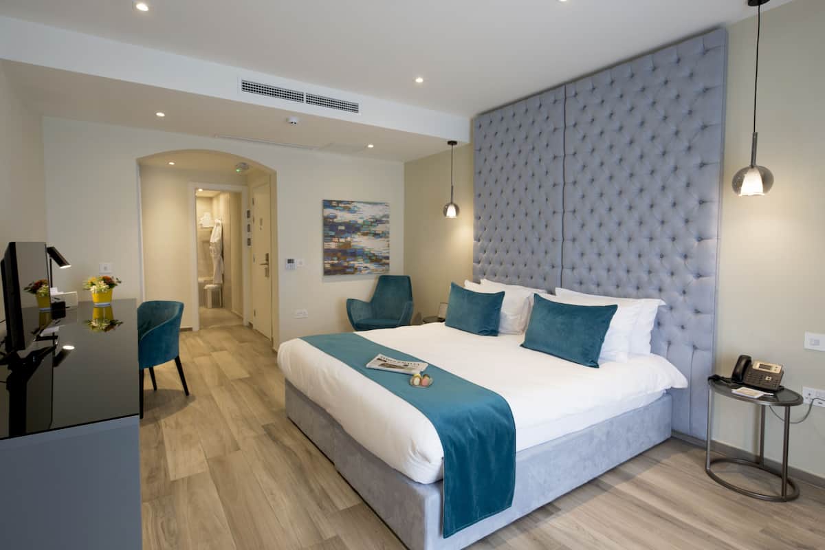 A modern bedroom with a large bed, a headboard, a bedside table with a phone, and a chair.