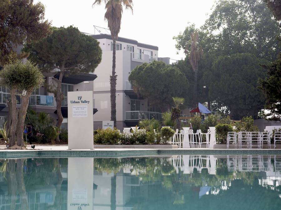 A swimming pool with a sign for Urban Valley, surrounded by trees and a building with balconies.