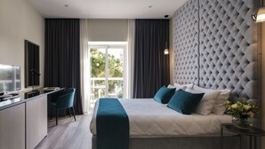 A modern hotel room with a large bed, a desk, and a view of greenery through the window. - Urban Valley Resort (San Gwann)